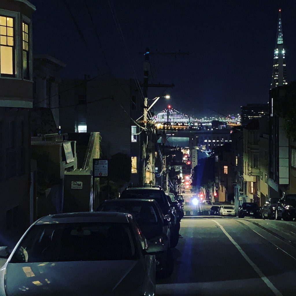 San Francisco at night, with Bay Bridge in background and cable car coming up hill